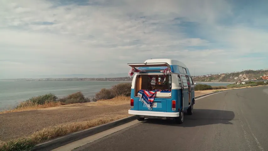 A blue campervan driving along a coastal road