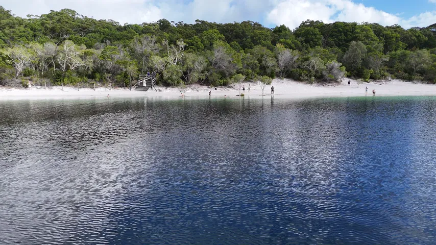 Aerial view of a calm freshwater lake edged with white sand and forest